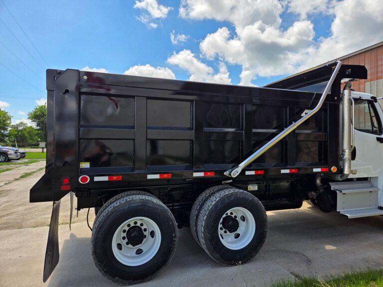 Side profile of a Freightliner Warren dump truck showing the glossy black FLS-14 body and tandem axles