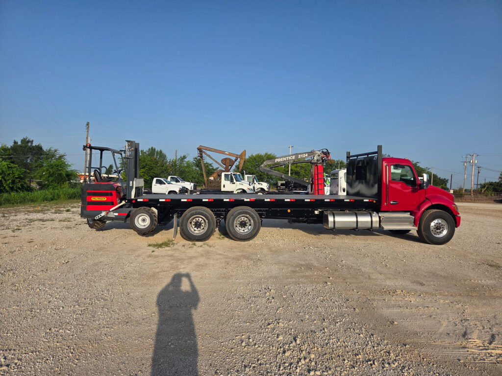 Side profile of a red Kenworth with a black Warren 24.5 foot stationary platform flatbed and a rear-mounted forklift