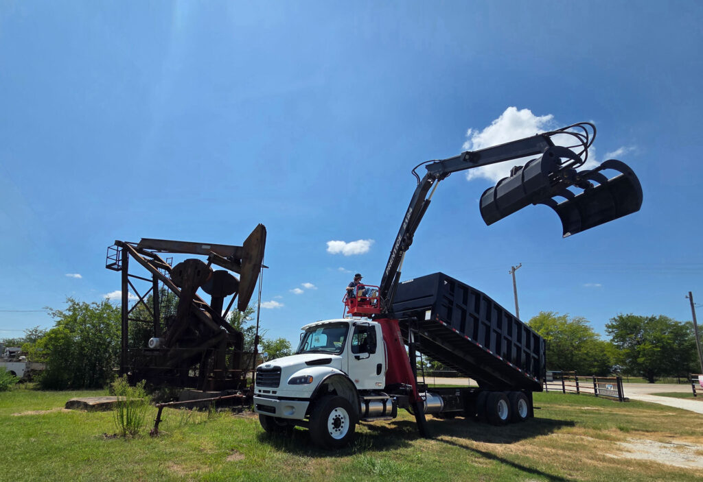 Operator running a Prentice 2124 knuckle grapple loader with boom extended over a Warren dump bed